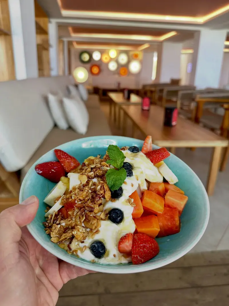 Bowl de frutas con yogur, granola, fresas, arándanos y papaya, con el salón del restaurante al fondo