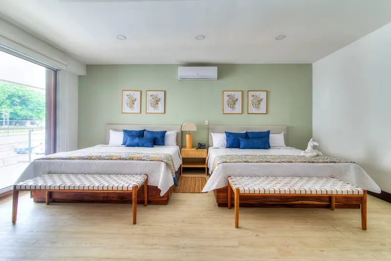 Suite con dos camas, sala con sofá y televisor, y ventanales a la terraza