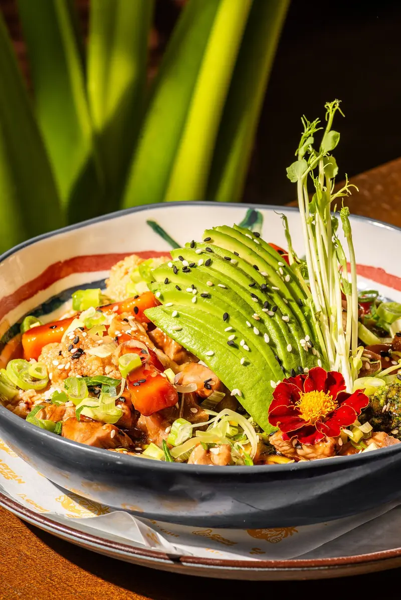 Bowl con vegetales, aguacate y flor roja sobre una mesa de madera
