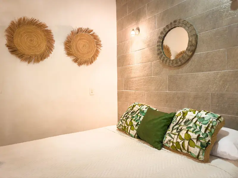 Cama con almohadones verdes y adornos de fibra natural en la pared