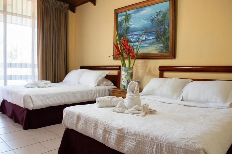 Habitación con dos camas, un cuadro de playa con palmeras en la pared y flores rojas en un florero