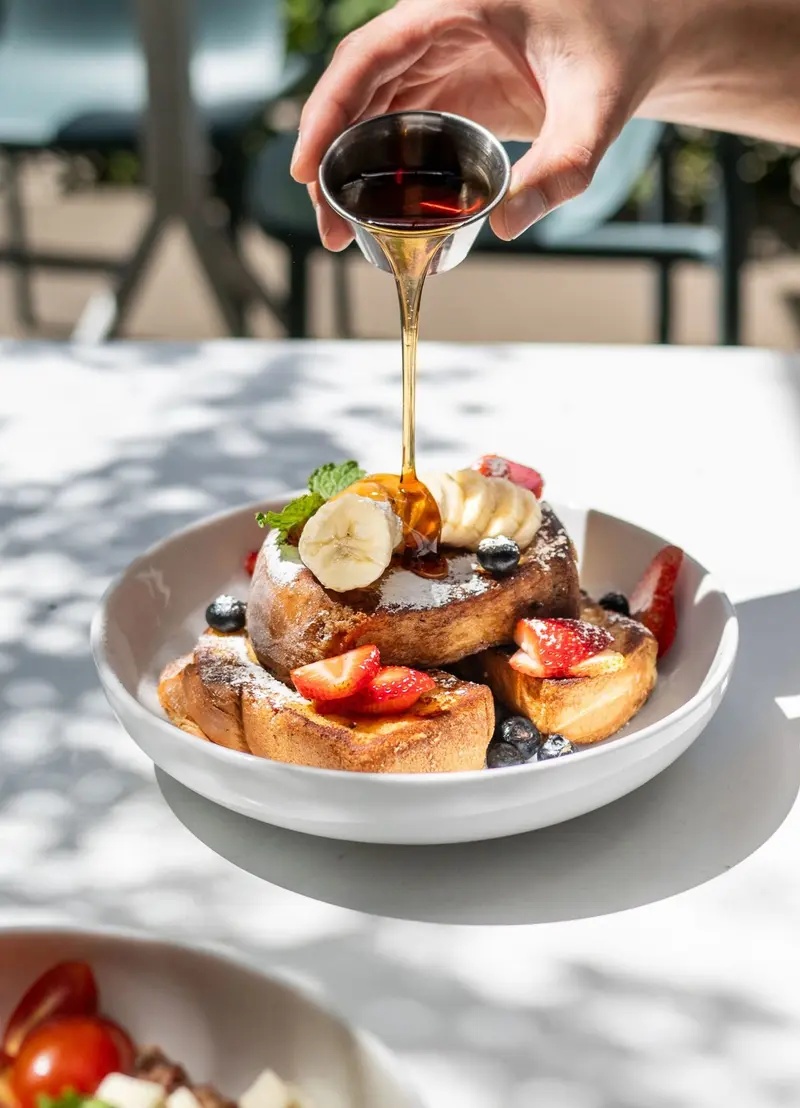 Tostadas francesas con fruta mientras se vierte sirope de maple desde un vasito