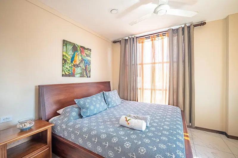 Habitación con cama de madera y ropa de cama azul, TV y ventana con cortinas