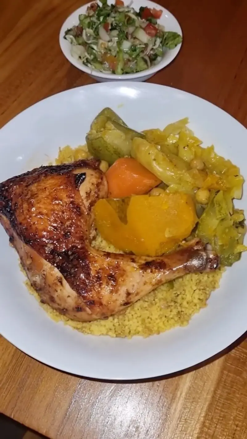 Muslo de pollo al horno sobre cuscús con vegetales, con una ensalada al fondo