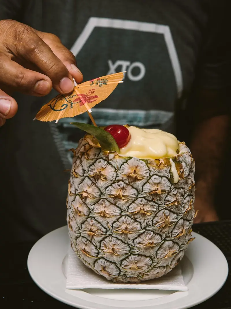 Cóctel servido en una piña con sombrilla de papel y cereza