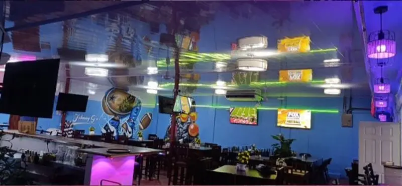 Salón con pantallas, mesas y barra bajo luces de colores