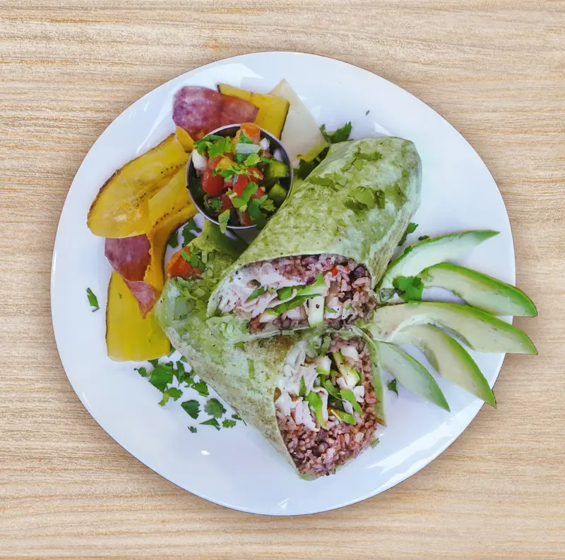 Wrap verde cortado por la mitad, con pico de gallo, plátano maduro y rodajas de aguacate