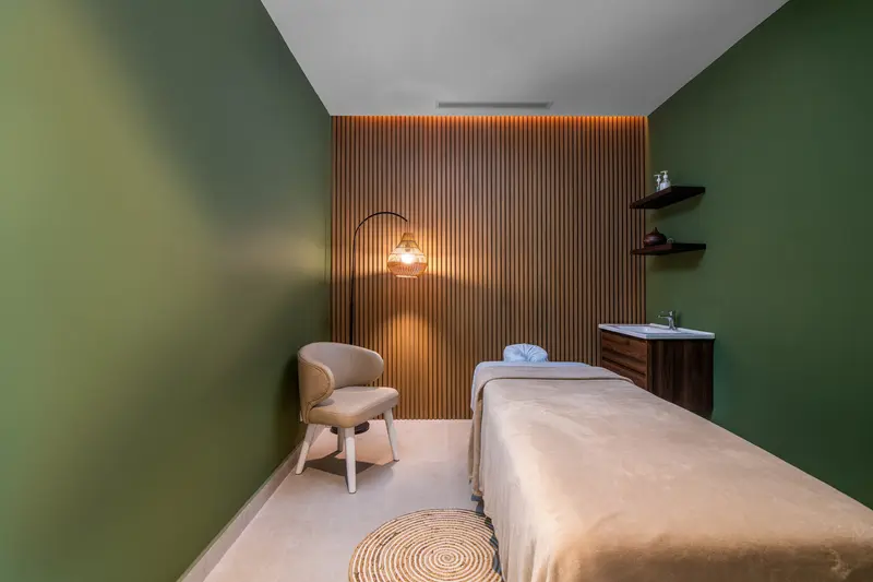 Sala de masajes con una camilla, paredes verdes y de madera y una lámpara