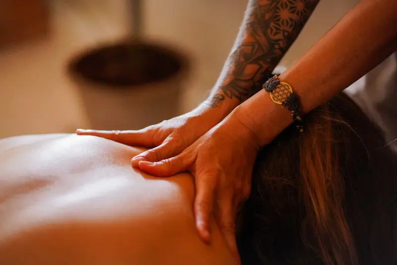 Manos tatuadas presionando la espalda de una persona durante un masaje