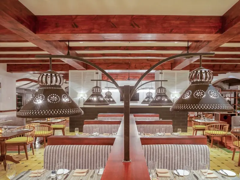 Comedor con techo de vigas de madera rojiza, lámparas de metal calado y bancos tapizados a rayas