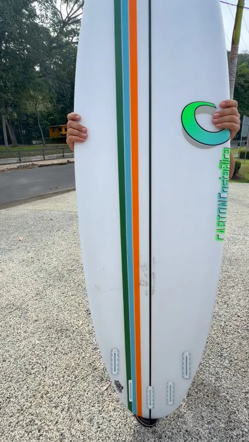 Tabla de surf blanca con franjas naranja y verde y el logo de Carton, sostenida en vertical