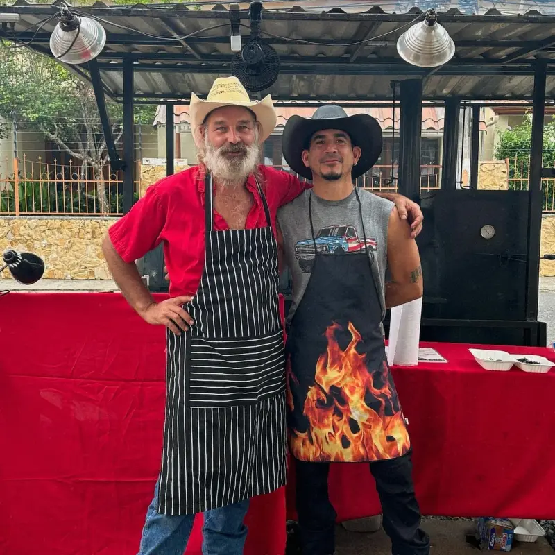 Dos cocineros con sombrero vaquero y delantal frente al ahumador