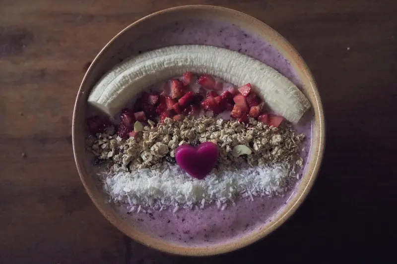 Bowl morado con banano, fresa y granola sobre una mesa oscura