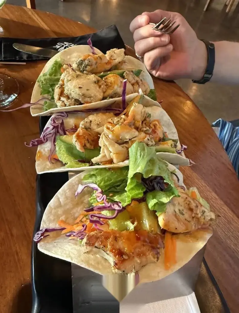 Tres tacos con camarones, repollo morado y salsa sobre una mesa de madera
