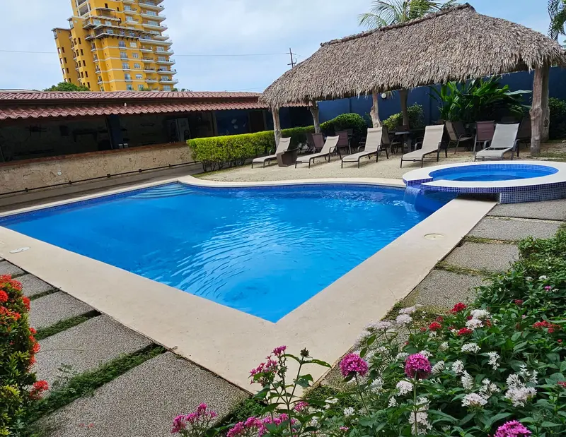 Piscina del hotel con un rancho de techo de paja y un jardín con flores