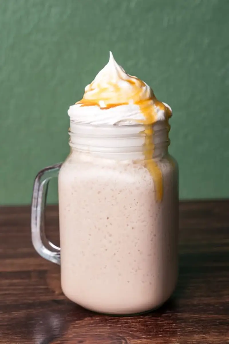 Malteada de caramelo en un vaso de vidrio con crema batida y salsa de caramelo