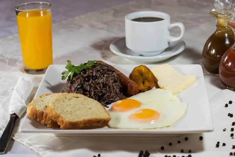 Desayuno con gallo pinto, huevos fritos, queso, pan, café y jugo de naranja