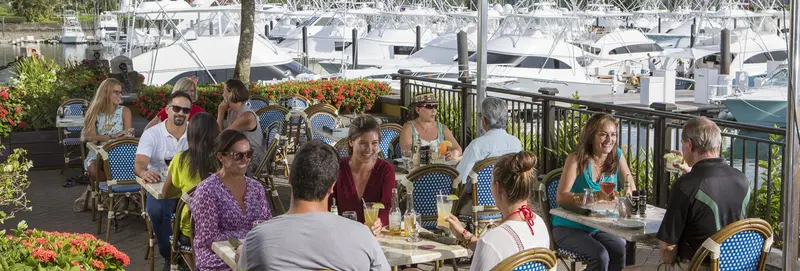 Mesas de un restaurante junto a la marina, con yates al fondo