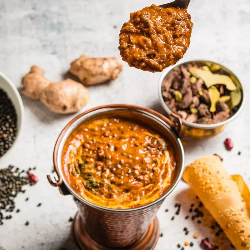 Daal makhani en un cuenco de cobre con papadum, jengibre y especias