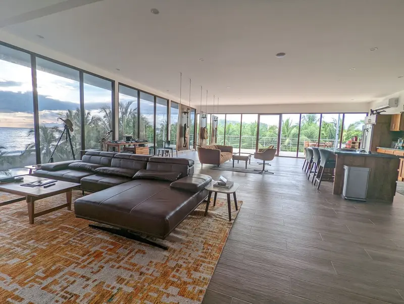 Sala amplia del penthouse con ventanales, sofá de cuero y cocina abierta