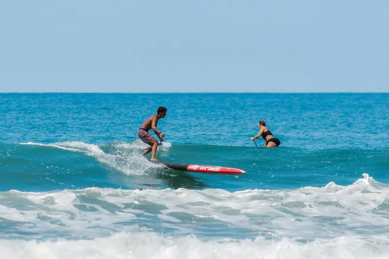 Remador de paddleboard surfeando una ola con una tabla roja