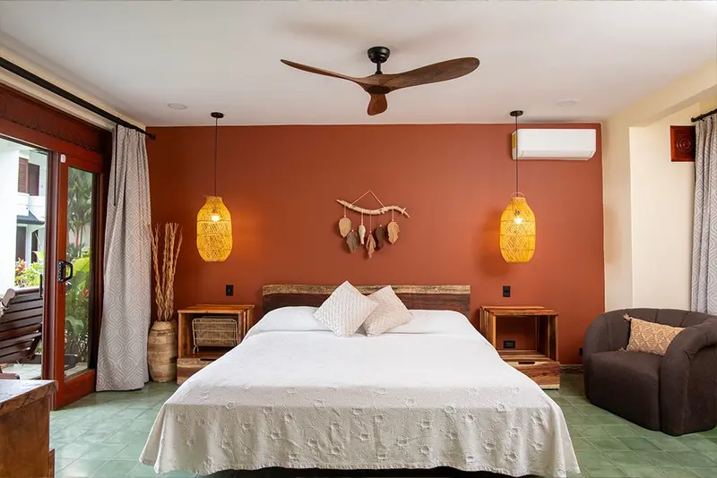 Dormitorio de un condominio con cama blanca, pared terracota, ventilador de techo y sillón