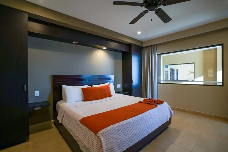 Habitación con cama king de cobija blanca y naranja, ventilador de techo y una ventana interior