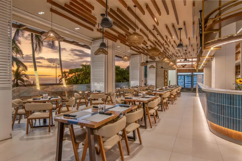 Restaurante con mesas de madera, techo de listones y una barra con azulejos azules al fondo