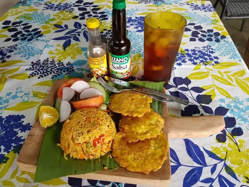 Almuerzo sobre una hoja de banano, con arroz, tortitas fritas y verduras, un vaso de té frío y una botella de salsa