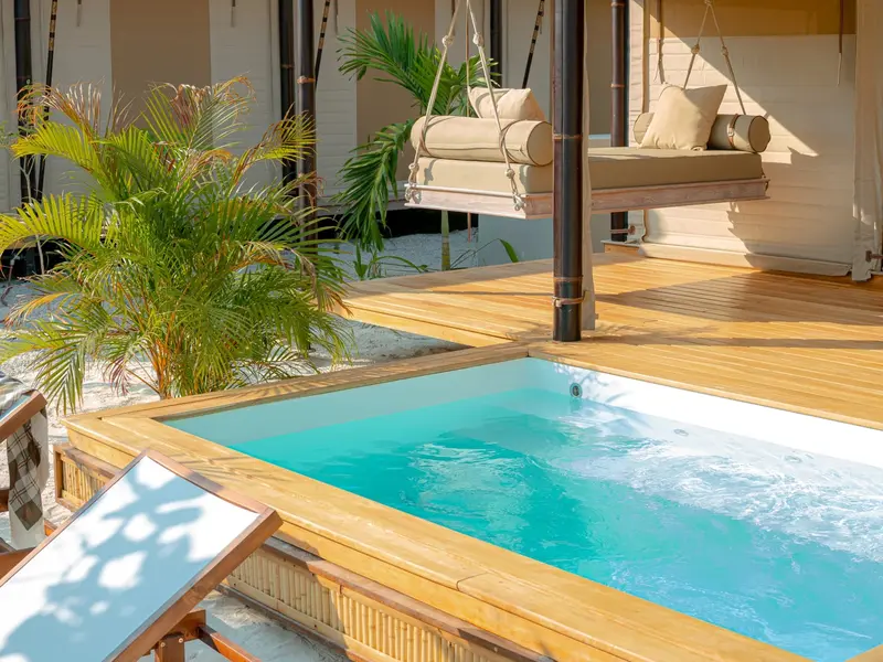 Piscina privada turquesa con una hamaca colgante y una reposera sobre una terraza de madera