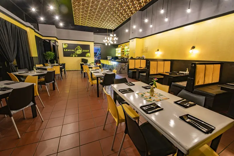 Salón con mesas blancas y sillas, y una barra con botellas al fondo