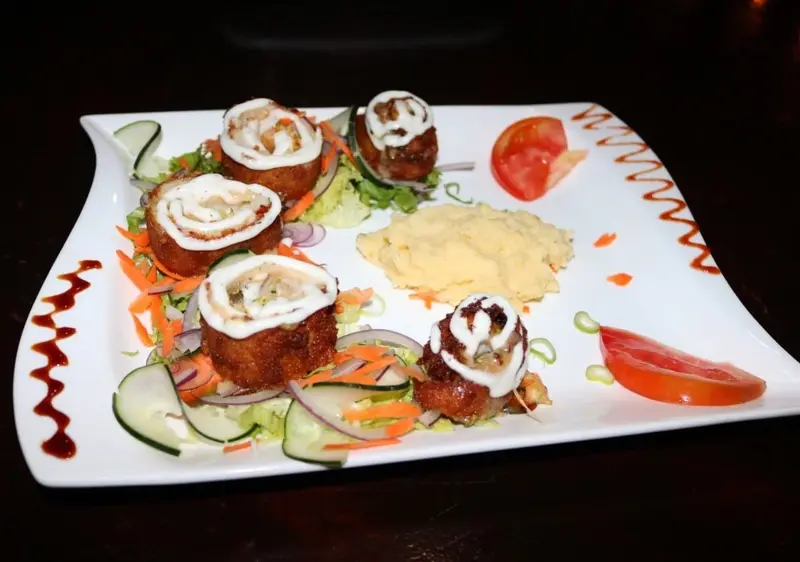 Plato blanco con filet de mahi mahi relleno enrollado, puré amarillo y ensalada