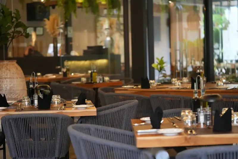 Salón de Zelva con mesas de madera, sillas de cuerda gris y ventanales hacia el jardín