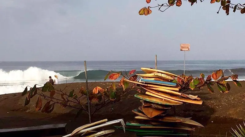 Tablas de surf apiladas sobre la arena negra, con una ola rompiendo al fondo