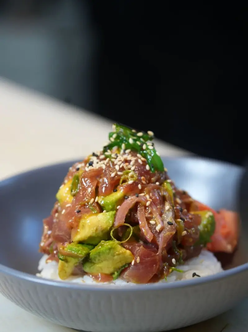 Ahi poke de atún con aguacate, algas y semillas de ajonjolí sobre arroz, en un bowl gris