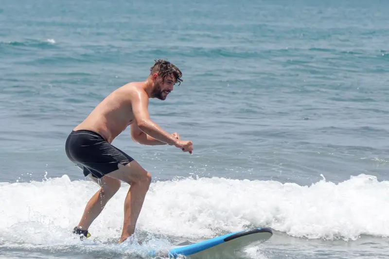 Surfista de pie sobre una tabla azul en una ola pequeña