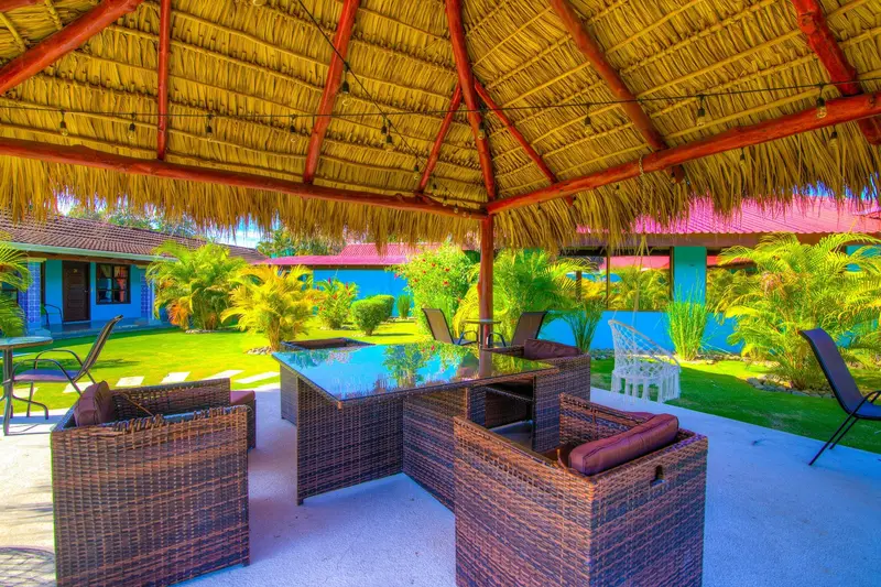 Palapa con techo de paja y muebles de mimbre junto al jardín