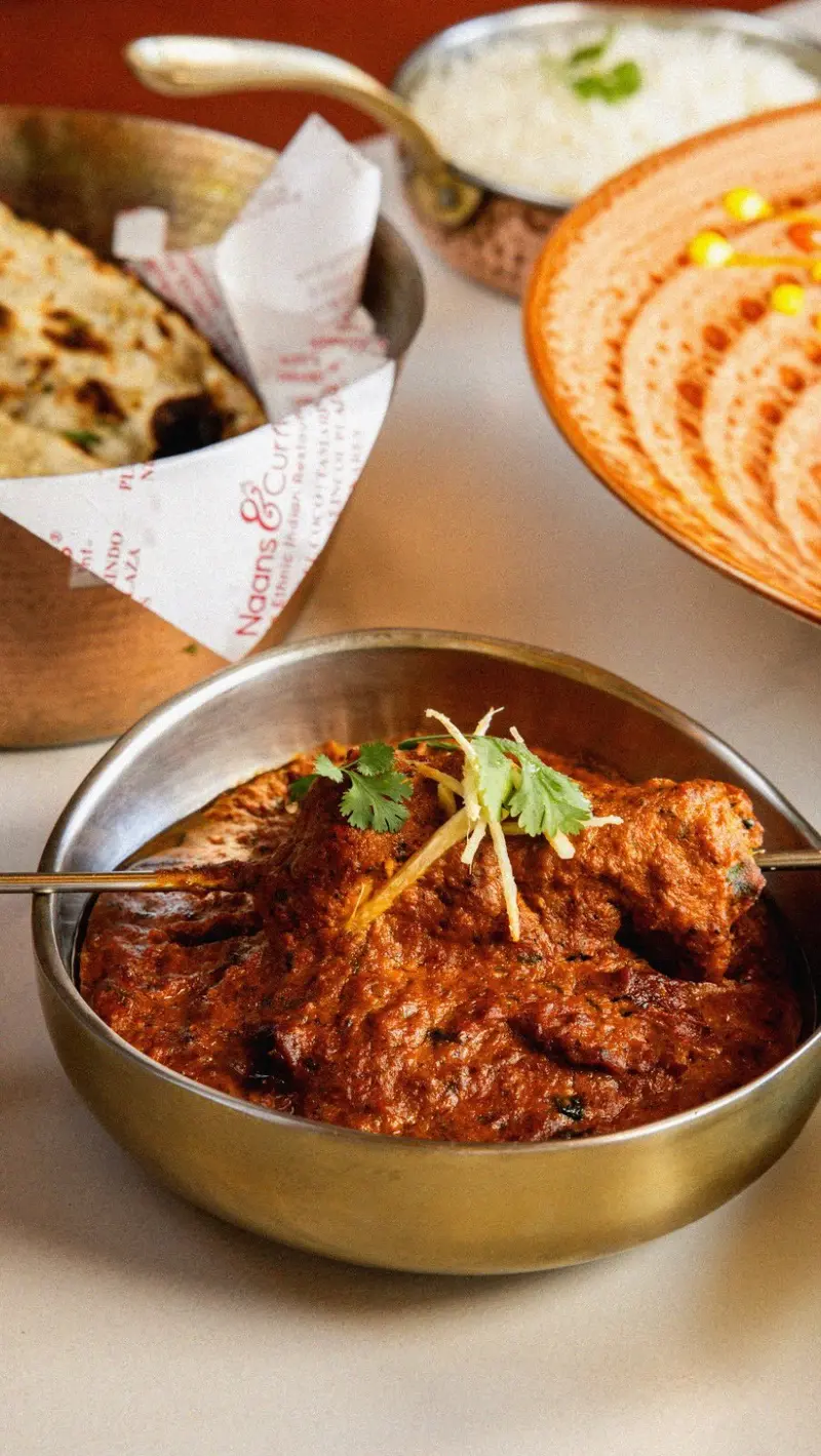 Curry de carne en un cuenco de metal con arroz basmati y naan en una cesta al fondo