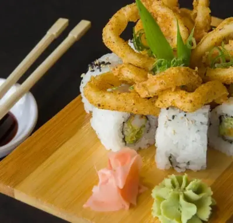 Rollos de sushi con aros de calamar fritos, jengibre y wasabi sobre una tabla de bambú