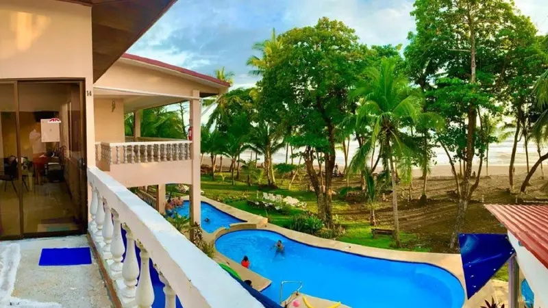 Vista desde un balcón del hotel hacia la piscina y los árboles frente a la playa
