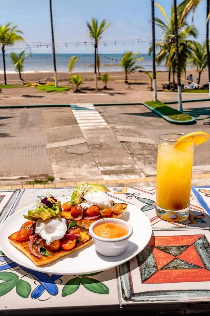 Desayuno servido en la terraza con jugo de naranja y la playa de fondo