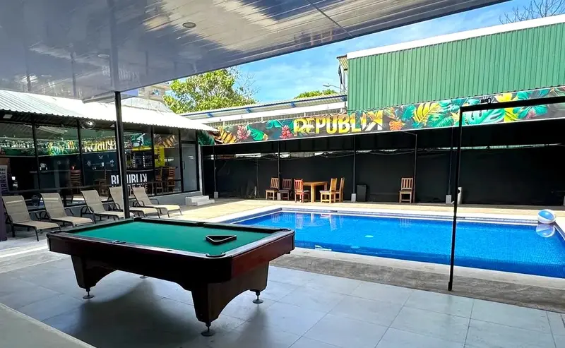 Mesa de billar junto a la piscina, con el mural de Republik y el bar al fondo