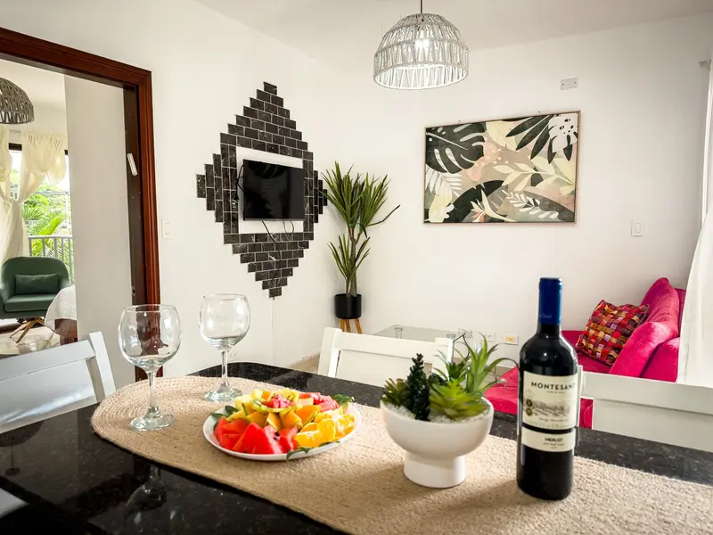 Sala de una suite con sofá rosado, televisor y mesa con vino y frutas