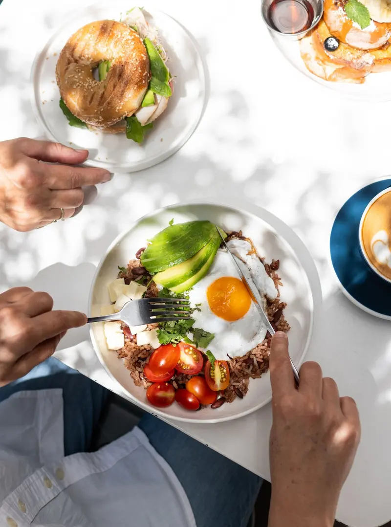 Desayuno visto desde arriba: huevos fritos, aguacate, tomates cherry, un bagel y un café