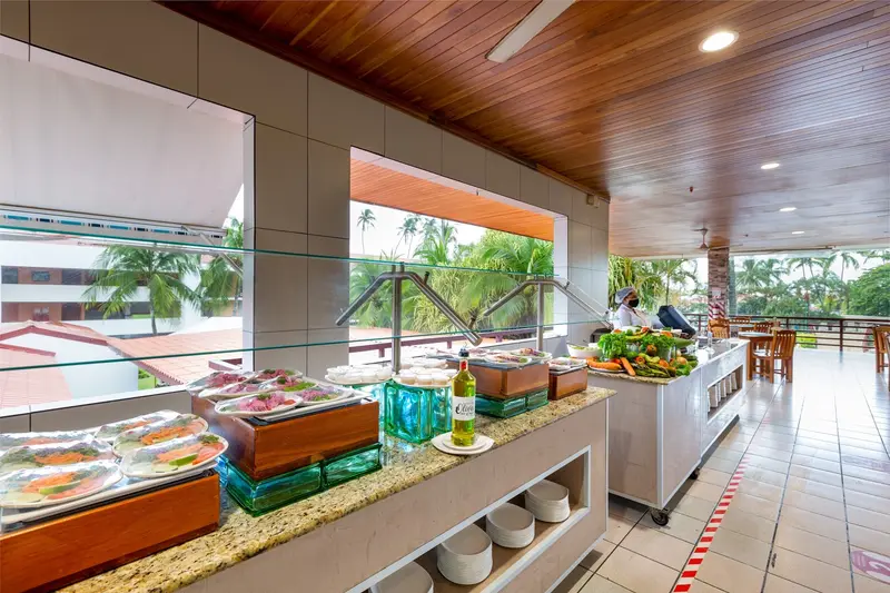 Estación de buffet con bandejas de ensaladas y platos fríos junto a ventanales abiertos