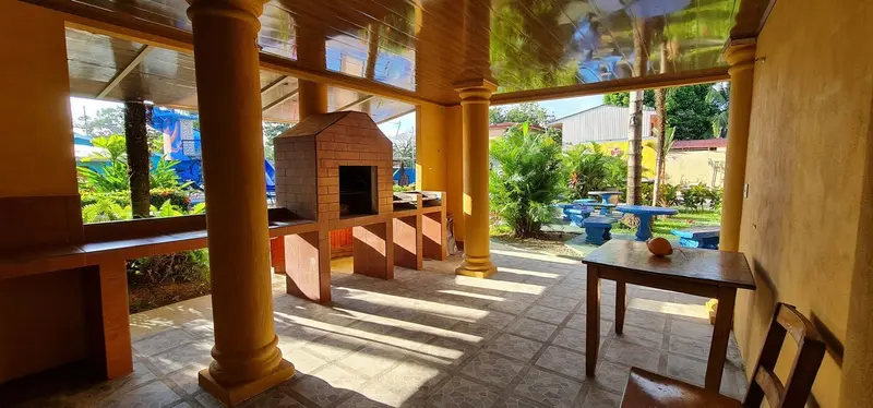 Área techada con horno de ladrillo y mesa de madera junto a la piscina
