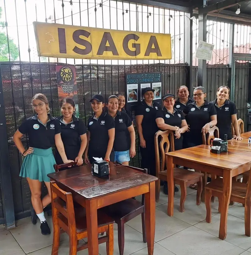 Equipo del restaurante posando entre las mesas de madera bajo el rótulo Isaga