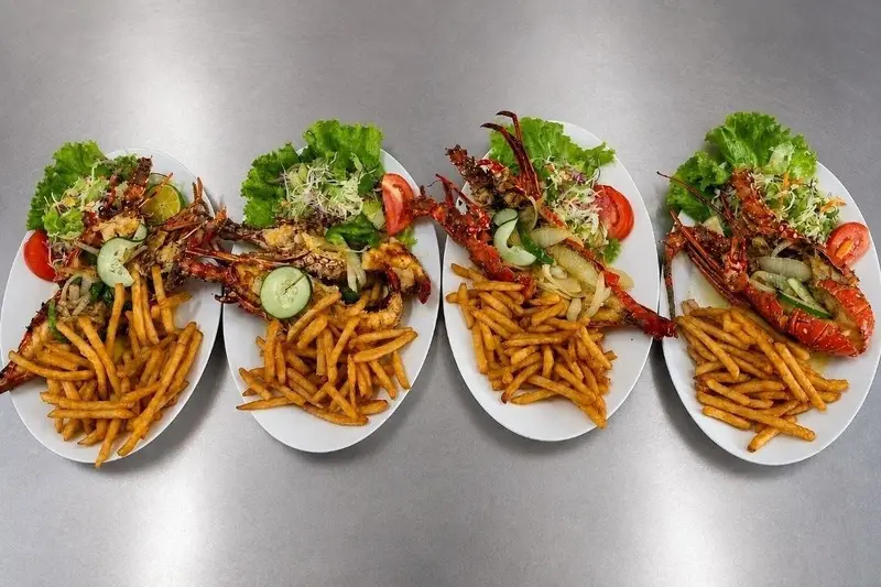 Cuatro platos de mariscos a la plancha con papas fritas y ensalada servidos en fila