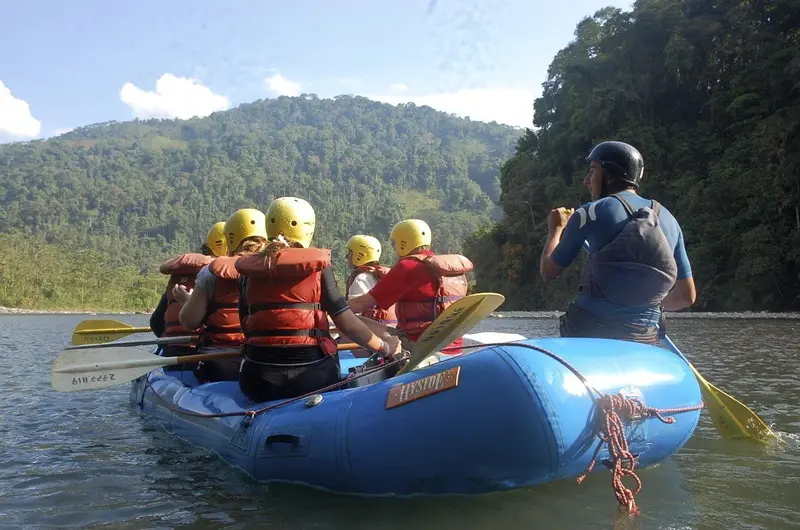 Guía y rafters de espaldas en una balsa azul sobre el río, con montañas cubiertas de selva
