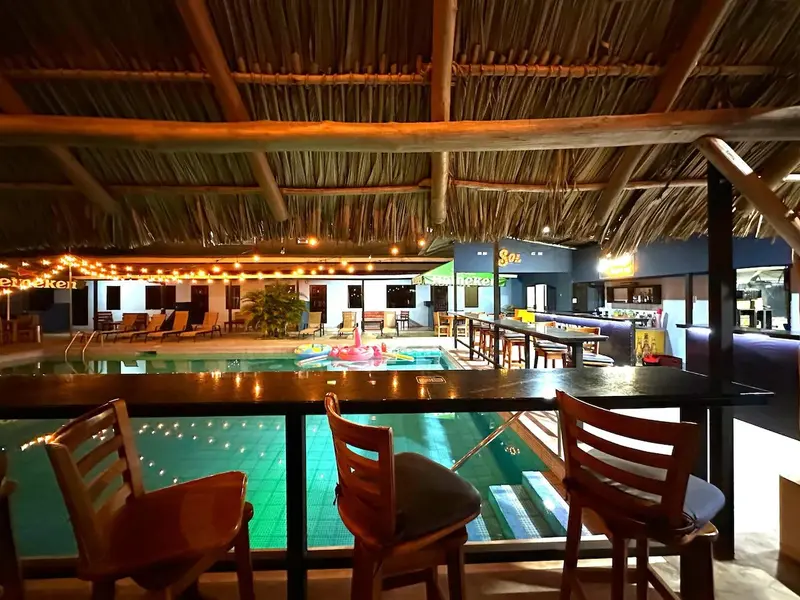 Vista de noche desde el segundo piso hacia la piscina iluminada y la barra con taburetes